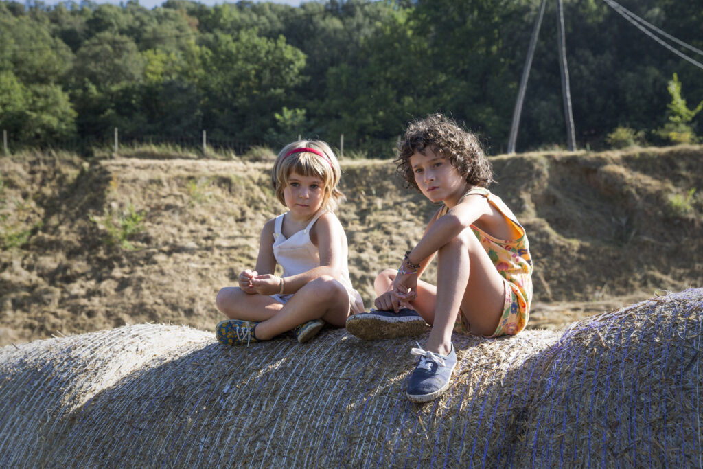 Frida und ihre kleine Cousine Anna sitzen auf einem Heuballen nahe dem Haus.