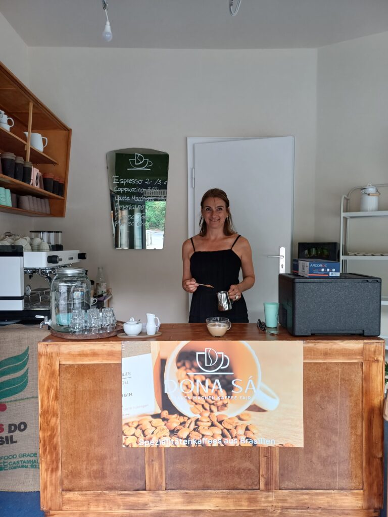 Inhaberin Adriana de Sá steht hinter dem Tresen und macht mit einem großen Lächeln im Gesicht einen Kaffee.